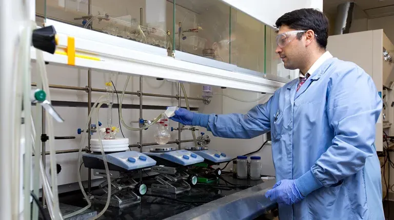 a pharmacy student wearing scrubs and safety goggles works in the lab